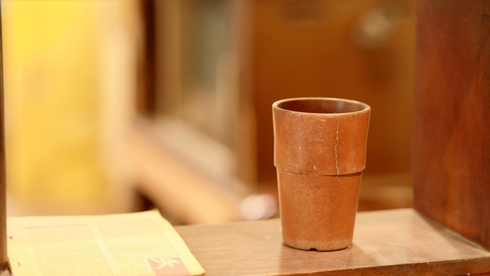 A reddish-brown unglazed Bizen ware tea cup on a wooden surface