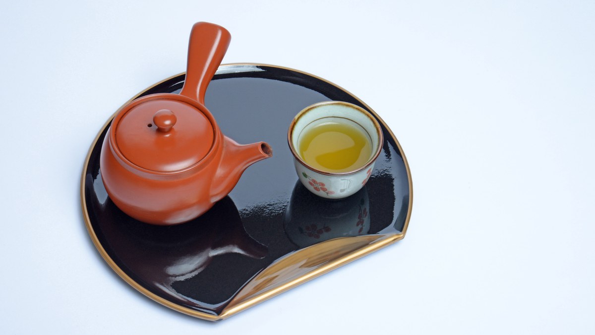 A red shudei kyusu seen from above beside a cup of green tea