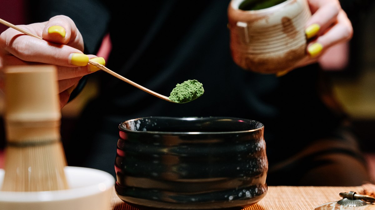 A bowl of bright green whisked matcha beside a cup of brewed green tea