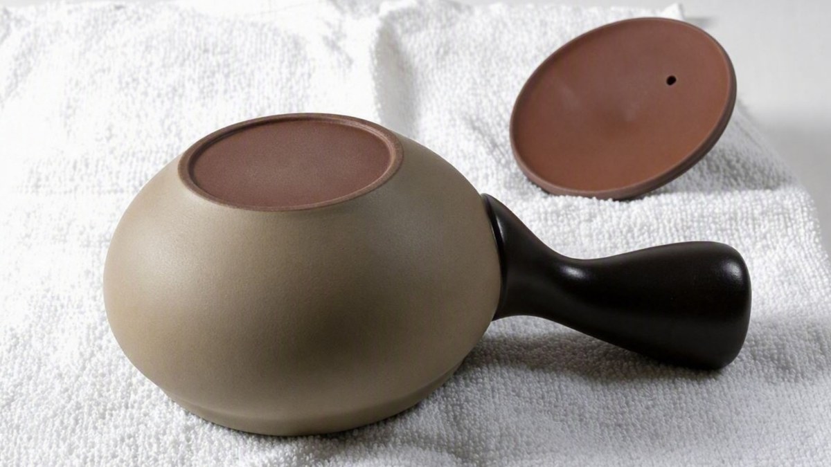 A Japanese clay teapot drying upside down with its lid off on a white cloth