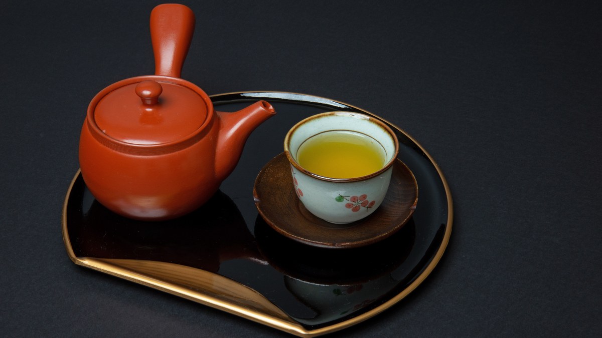 A red shudei kyusu and a cup of green tea on a black lacquer tray