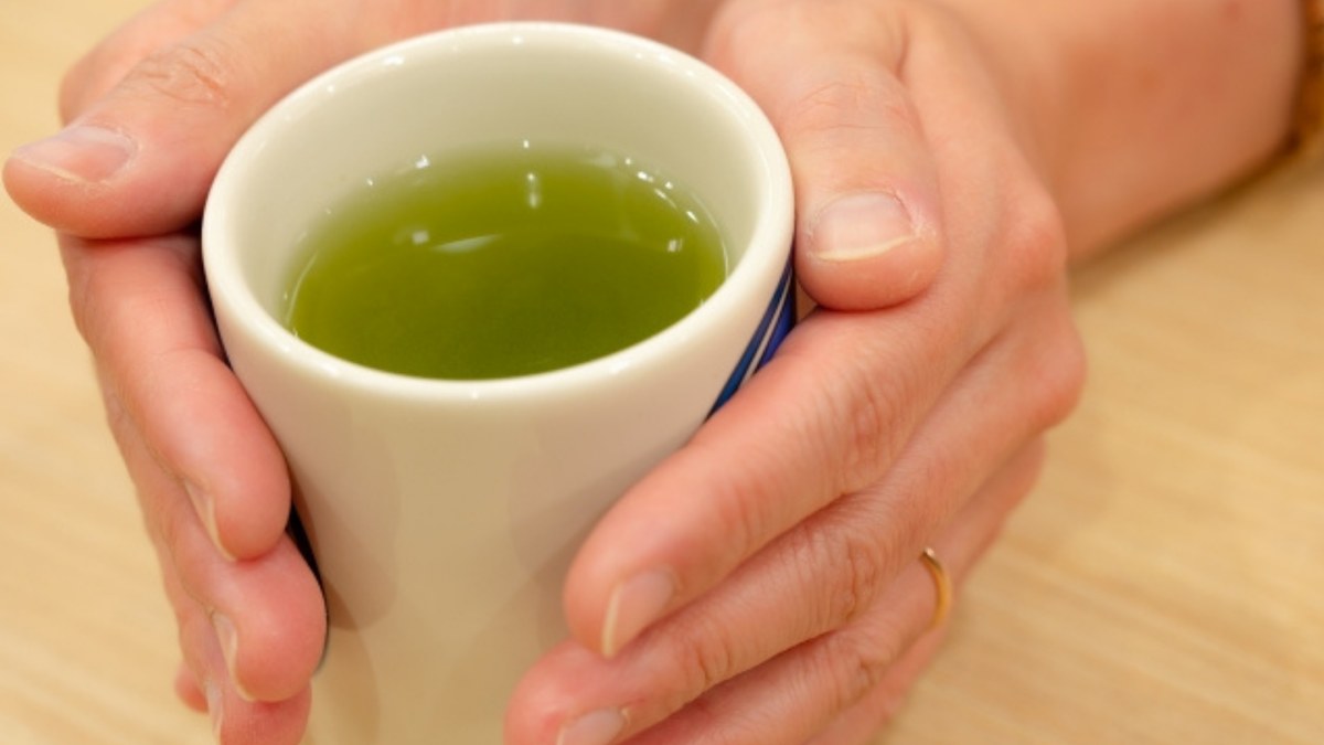 Two hands cupping a Japanese yunomi filled with green tea