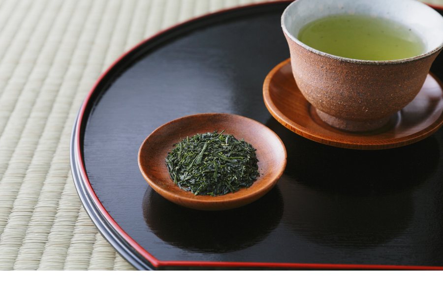 A simple Japanese kyusu teapot beside a cup of green tea