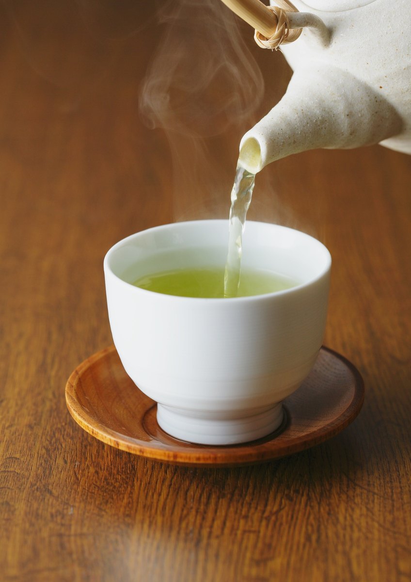 Green tea poured into a cup with steam rising