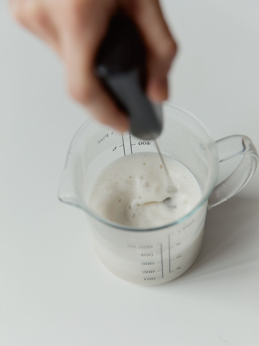 Frothing warm milk into a soft foam with a handheld frother