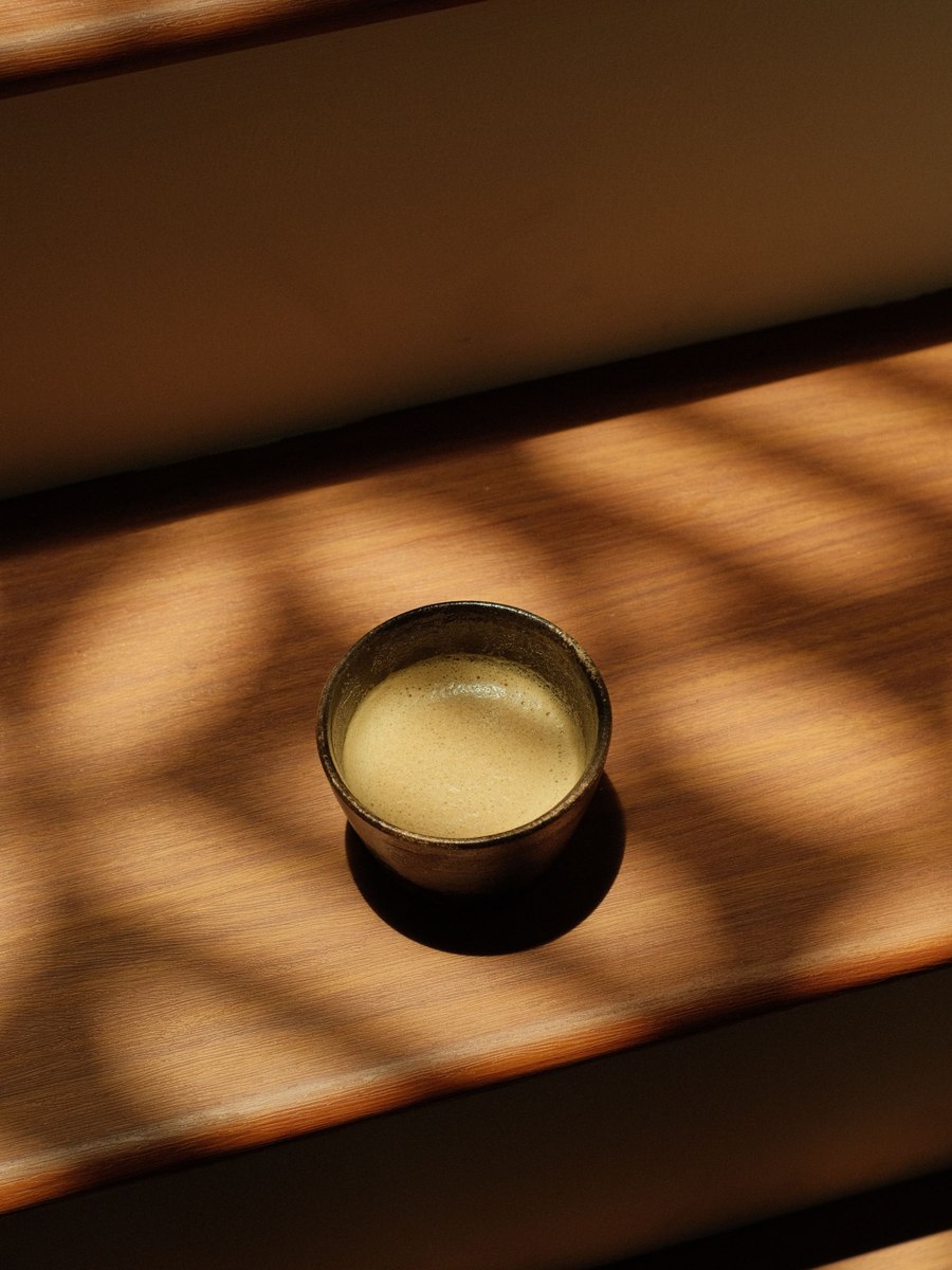 A small cup of hojicha resting in soft slatted sunlight on a wooden surface