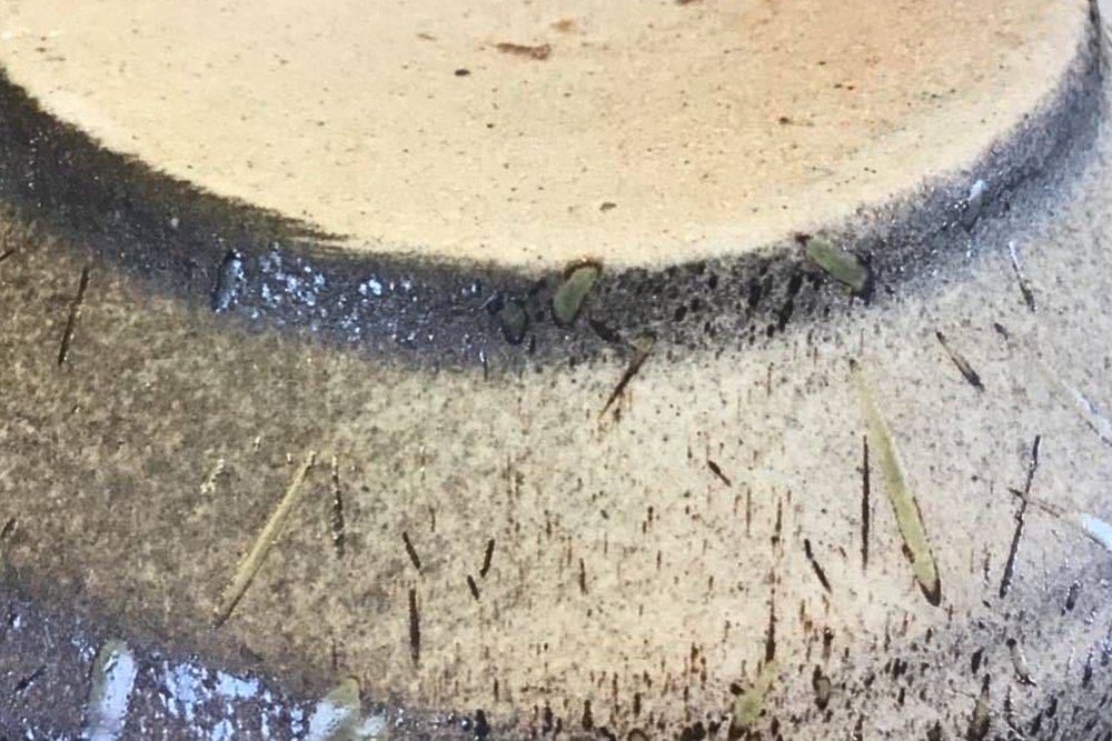The dark scorched foot of a Shigaraki bowl, with fine straw marks across the body