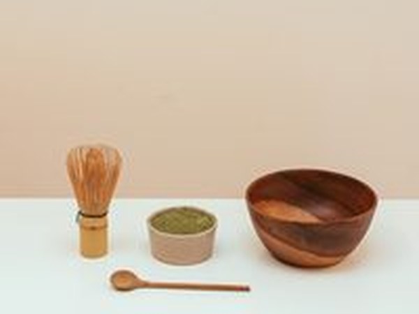 A bamboo whisk, a bowl of matcha and a wooden dish