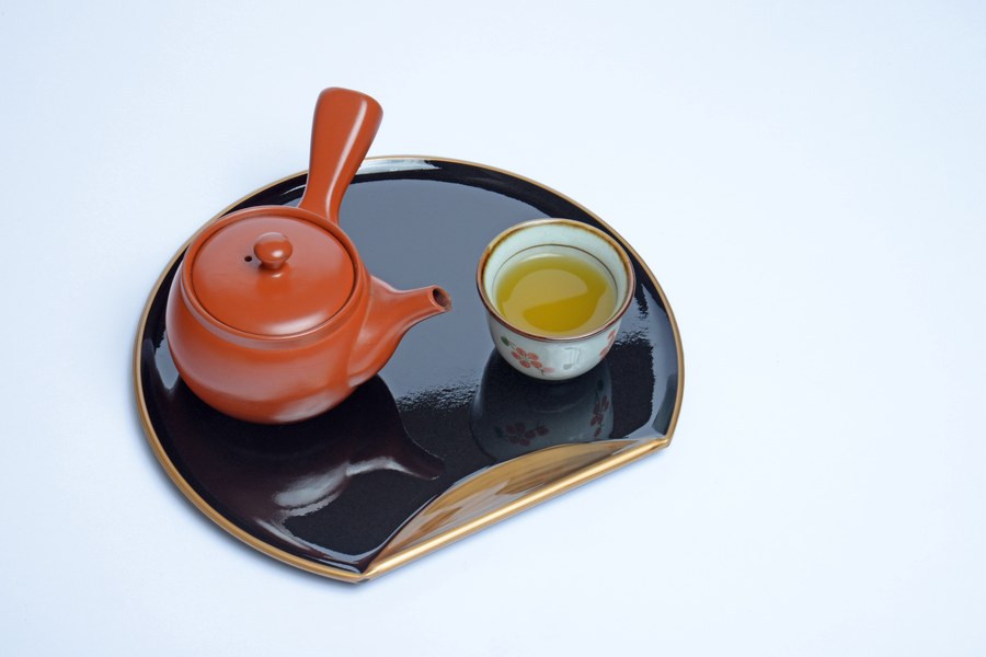 A red shudei kyusu seen from above beside a cup of green tea