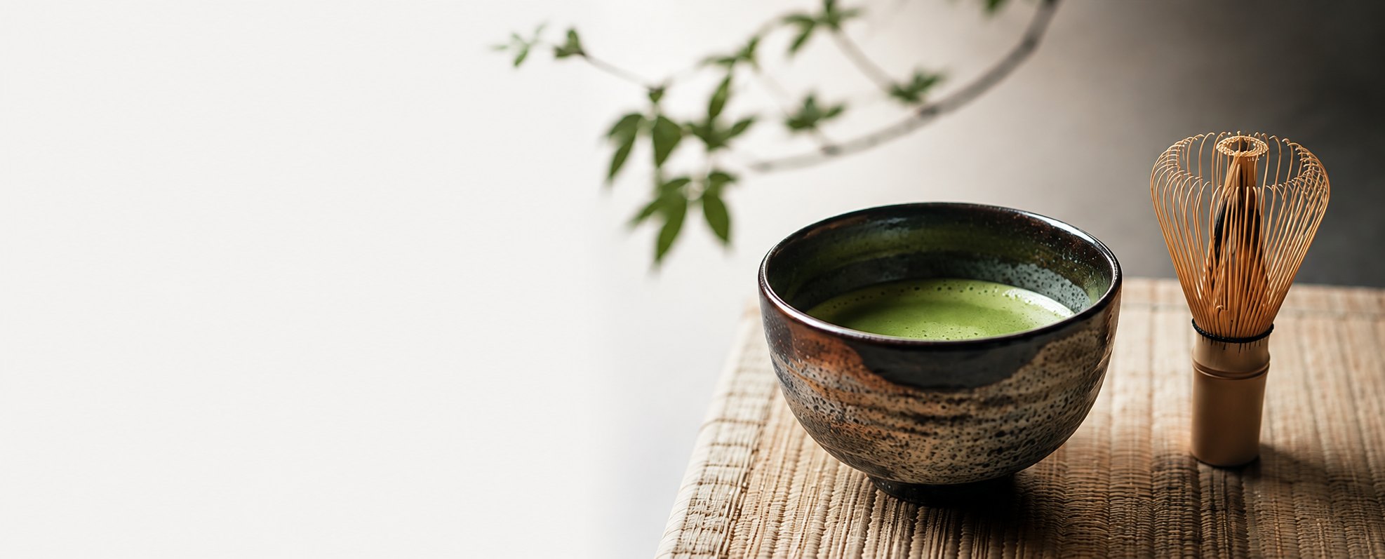 A bowl of whisked matcha beside a bamboo whisk on a woven mat