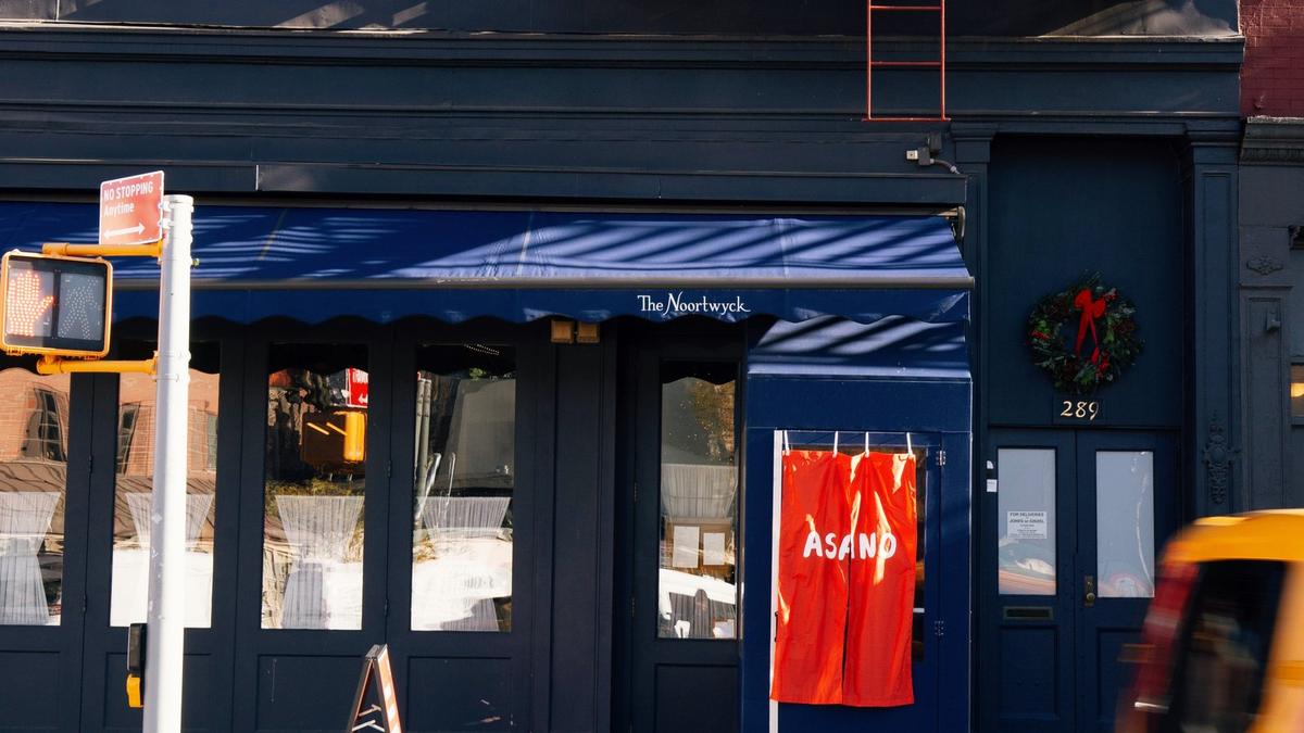 An orange ASANO noren beside the side door of The Noortwyck in the West Village