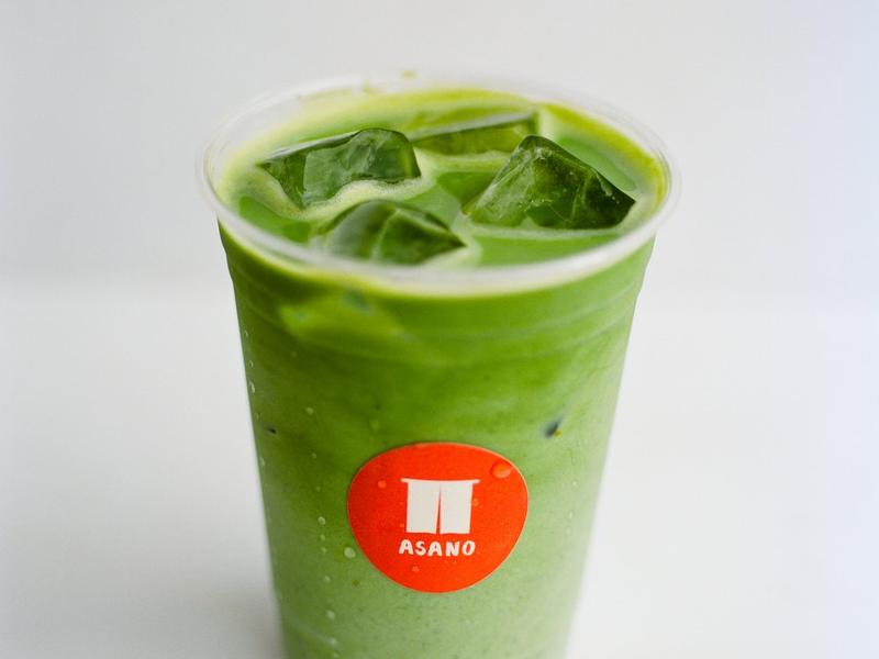 An iced matcha latte in a clear cup with an orange ASANO sticker