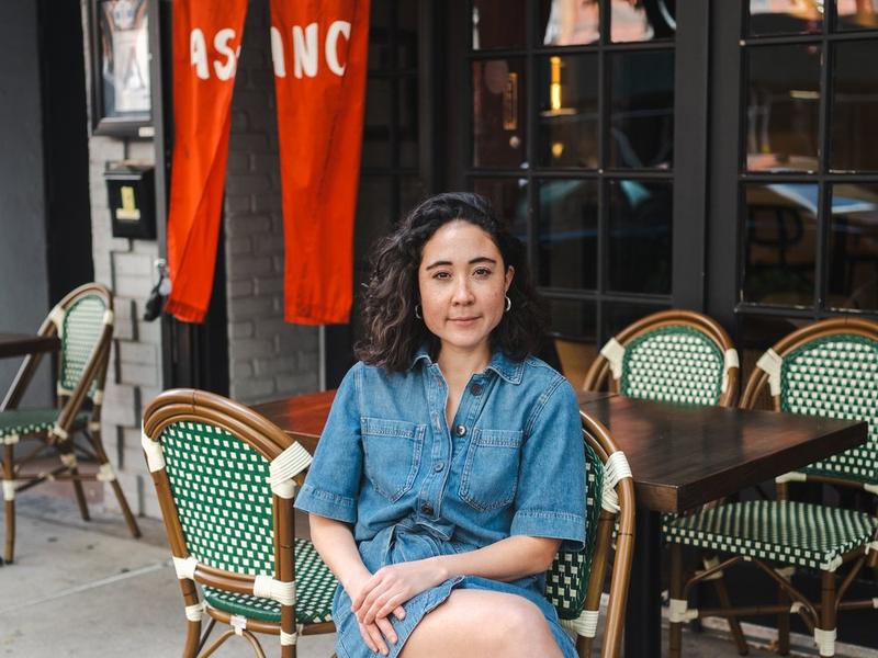 Kate Asano seated at a sidewalk table outside the shop